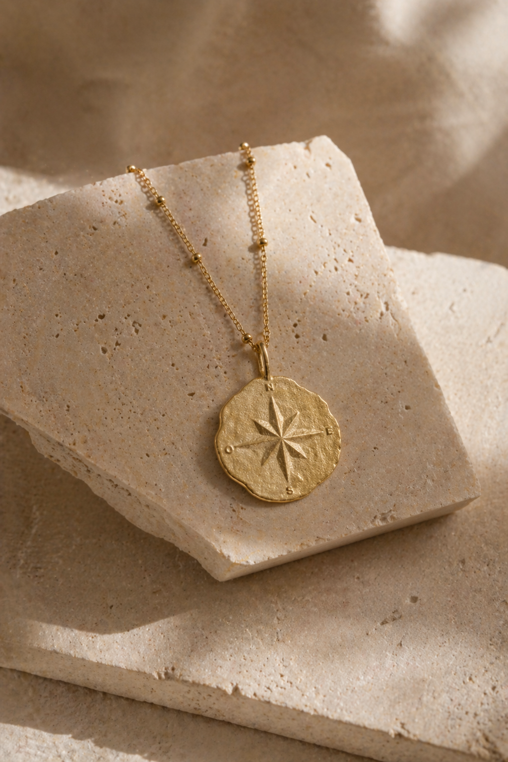 Gold necklace with a  compass star pendant on a textured beige surface 24K gold 