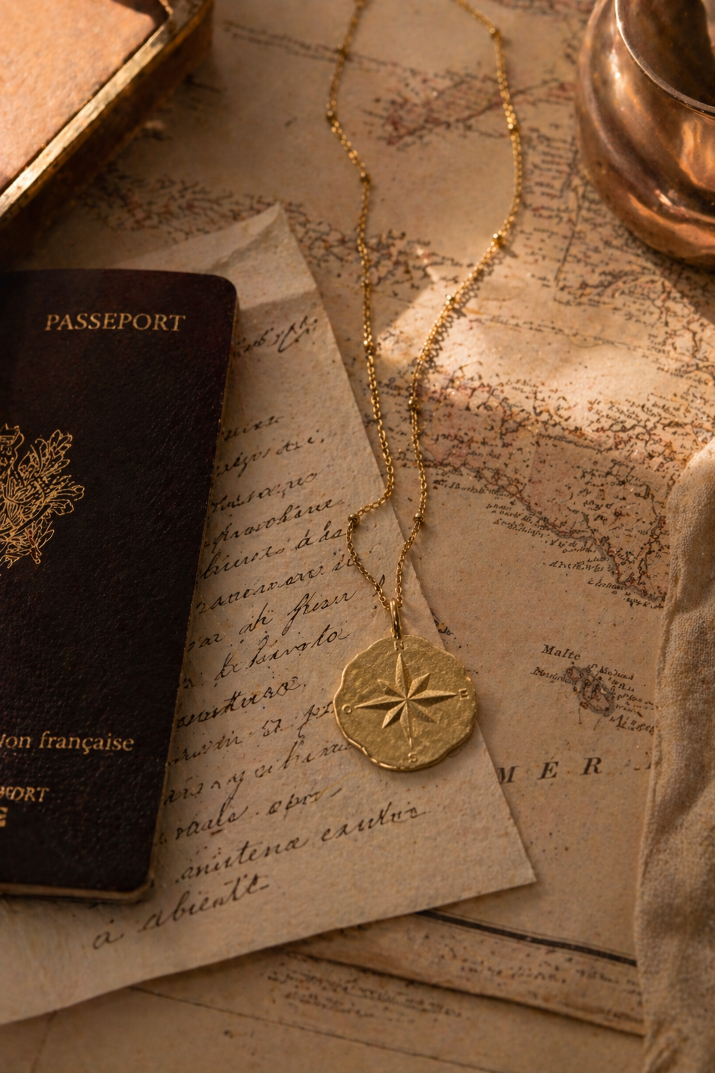 24K Gold necklace with a compass pendant on top of an old map and passport Made in France
