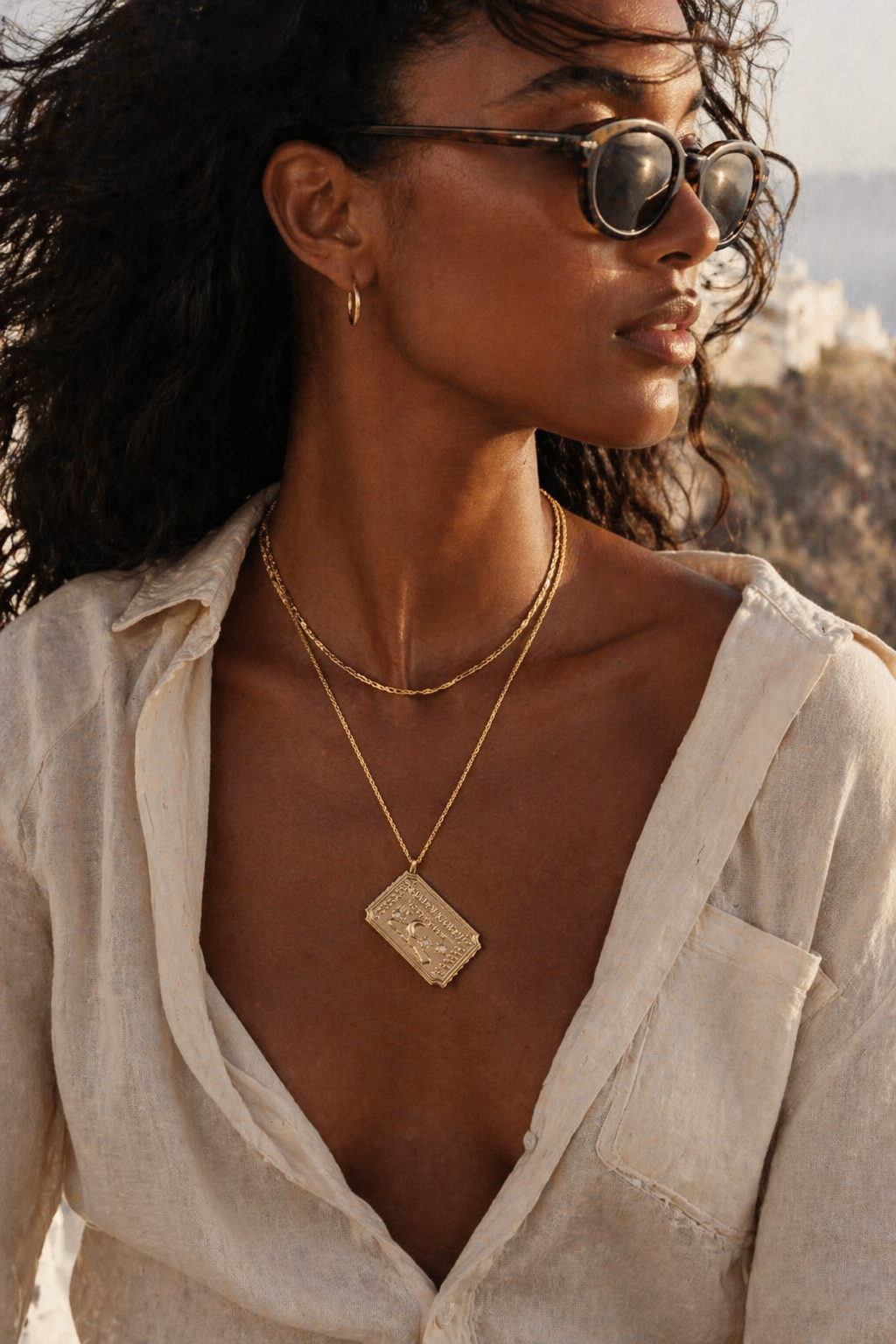 Woman wearing sunglasses and a golden ticket to the moo necklace by Bittersweet Jewelry sold by inner sanctum (a scenic background)