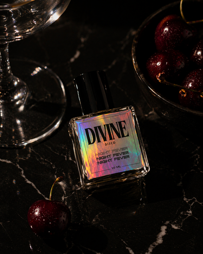 Perfume bottle labeled 'DIVINE disco' with cherries and a glass on a dark surface